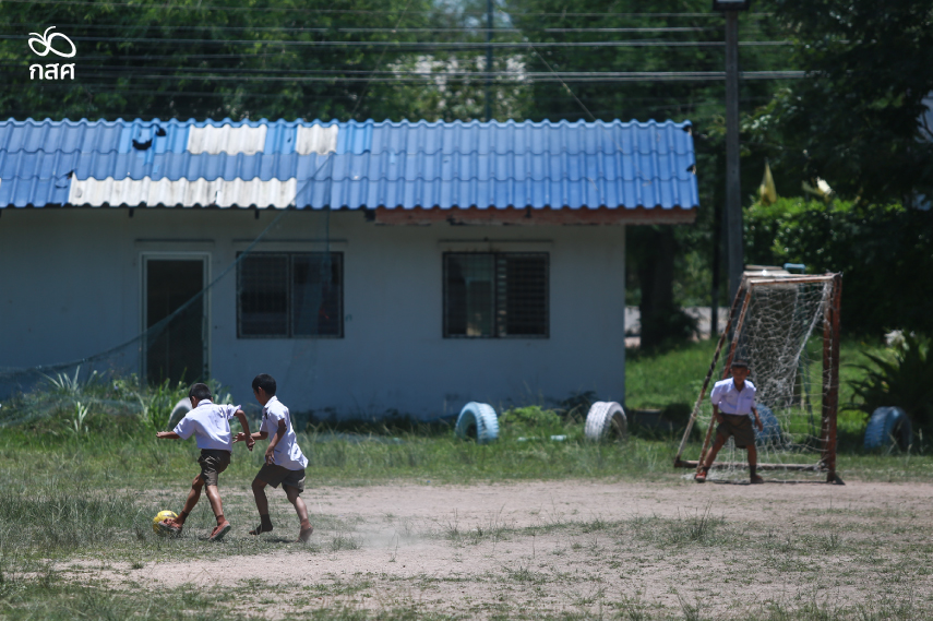 เด็กนักเรียน 3 คนเล่นลูกฟุตบอลกันในสนามหญ้ารกร้าง